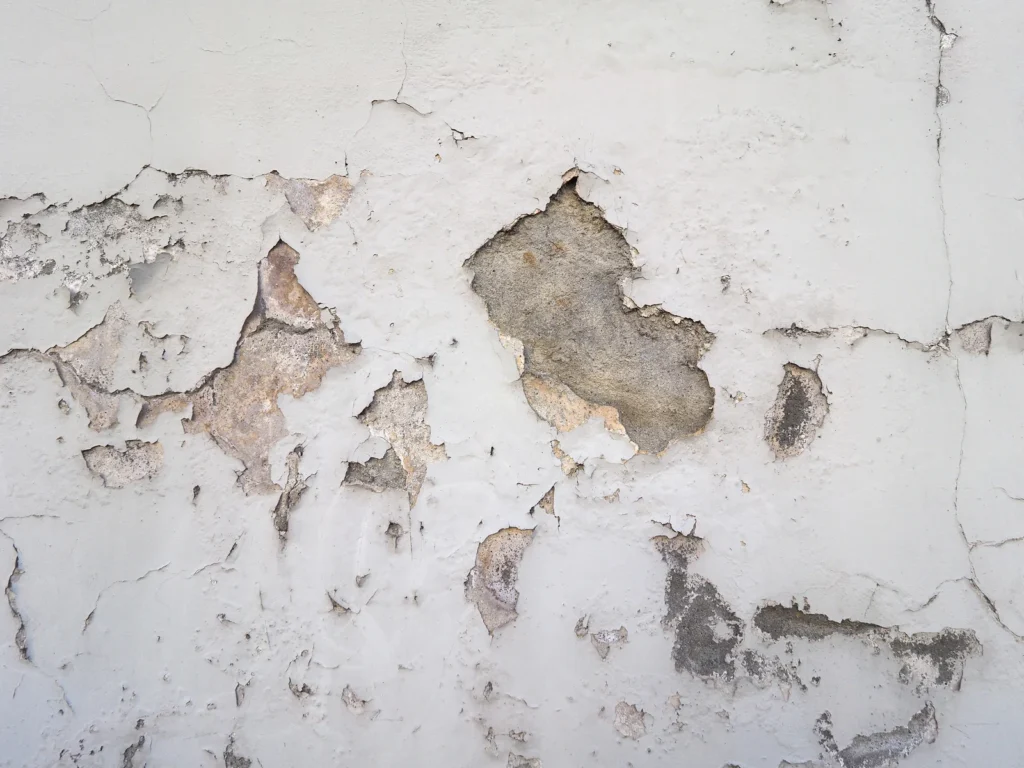 Peeling paint and cracked plaster on a damaged wall caused by moisture and water intrusion